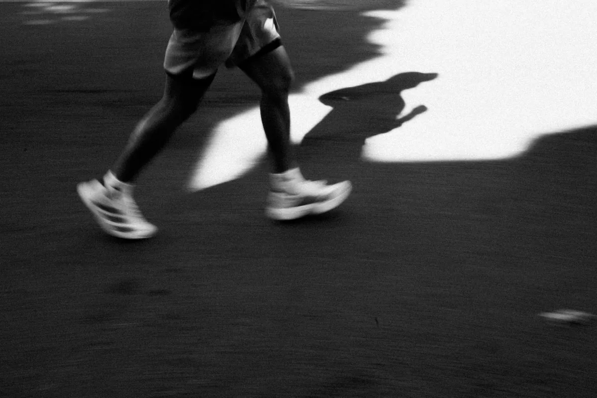 A runner's legs and shoes in motion, blurred, with a long shadow on the pavement